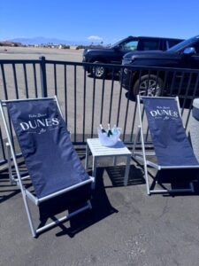 Custom navy blue sling chairs featuring white "Dunes Private Air" logos on the backrest, placed in a sunny outdoor VIP airfield lounge.